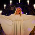 Adventsmarktengel Johanna (2024) Blondes Mädchen im weißen Gewand steht vor einem großen Kerzenleuchter