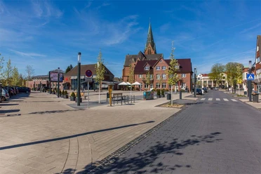 Wochenmarkt Sögel 1 Marktplatz in Sögel mit Kirche im Hintergrund, Sitzbereich und Bäumen unter blauem Himmel