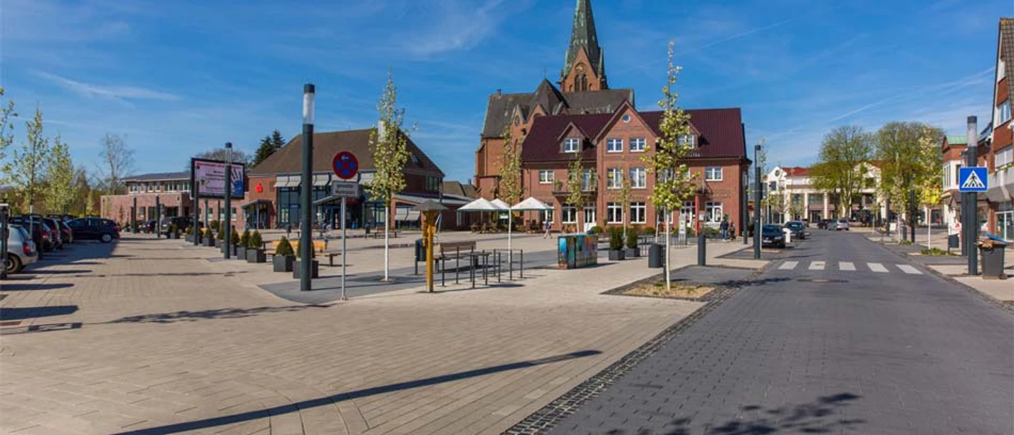 Wochenmarkt Sögel 1 Marktplatz in Sögel mit Kirche im Hintergrund, Sitzbereich und Bäumen unter blauem Himmel