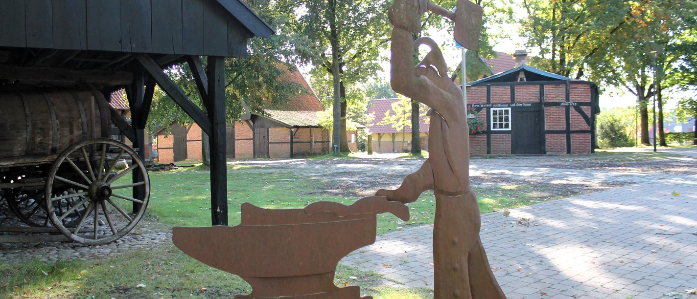 Wagenremise, Scheune und Backhaus – Heimathof Emsbüren ©Emsland Tourismus GmbH.JPG Metallskulptur eines Schmieds vor historischen Fachwerkgebäuden im Heimathof Emsbüren.