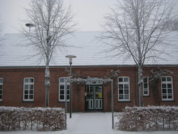 Dörpshus Tange im Winter Backsteingebäude mit weißen Fenstern im Winter, verschneite Bäume und Hecke davor.