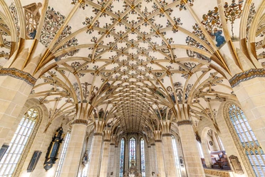 Gotisch kerkinterieur met prachtige netgewelven en versierde plafonds, warme aardetinten.