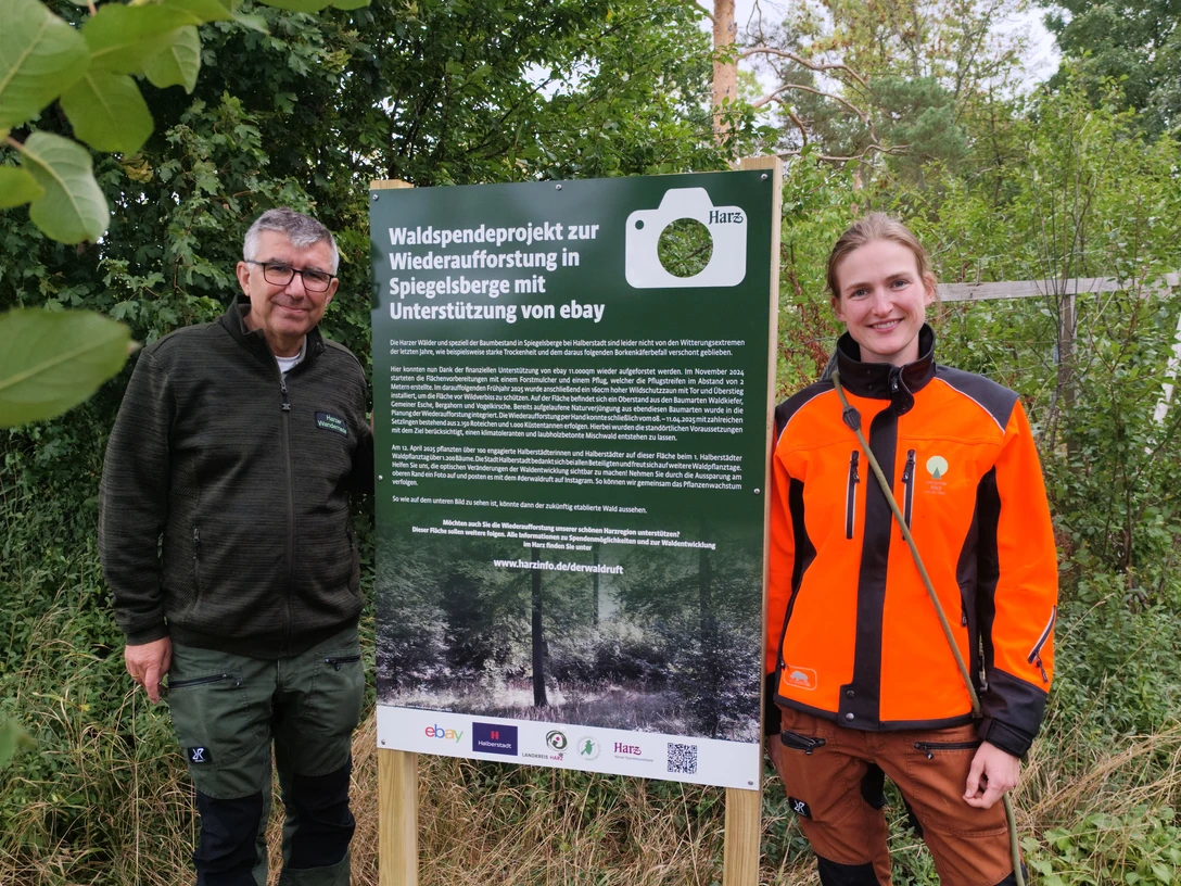 Fotospot Spiegelsberge Zwei Personen stehen im Grünen neben einem Schild zum Waldspendeprojekt Spiegelsberge.