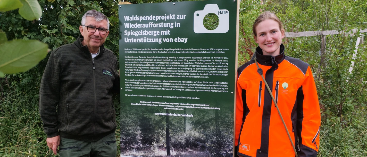 Fotospot Spiegelsberge Zwei Personen stehen im Grünen neben einem Schild zum Waldspendeprojekt Spiegelsberge.