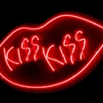 KISS KISS (c) Shu Lea Cheang.jpg Leuchtende Neonlinien in Form von einem Mund mit "KISS KISS" in kräftigem Rot auf schwarzem Hintergrund.