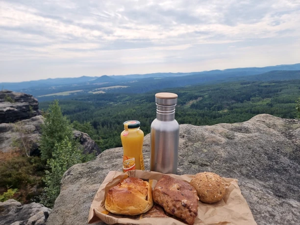 Picnic on a rock with a view of wooded hills, including pastries and drinks.