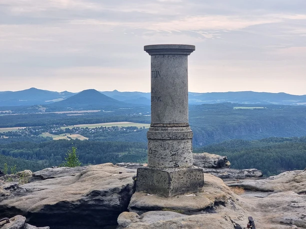 Großer Zschirnstein Aussicht Steinsäule auf Felsplateau mit Aussicht auf bewaldete Hügel im Hintergrund.
