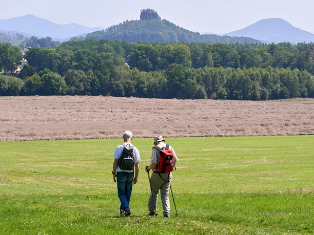 Two hikers in a meadow with a circle stone in the background.