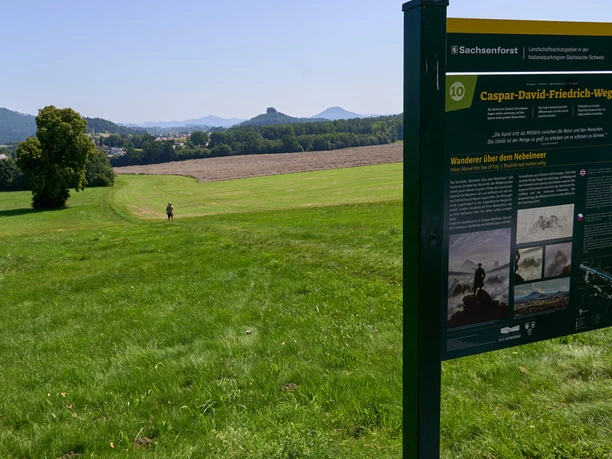 Caspar David Friedrich informatiesteen op de voorgrond, landschap met velden en heuvels op de achtergrond.