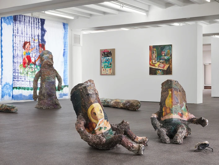 Amelie von Wulffen, Installationsansicht Eine Ausstellungsansicht mit bemalten Skulpturen und farbenfrohen Gemälden in einem hellen Raum.An exhibition view with painted sculptures and colorful paintings in a bright room.