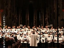 Kirchenchor in weißen Gewändern singt in einer beleuchteten Kathedrale.