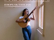 Steph Strings spielt Akustikgitarre. Im Raum fällt Licht durch ein Fenster.