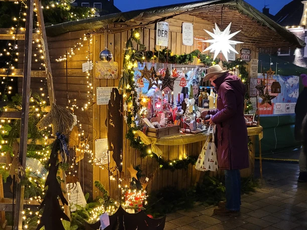 Weihnachtsmarkt in Radevormwald Weihnachtsmarktstand im Abendlicht, dekoriert mit Lichterketten, Besucher in Wintermantel.