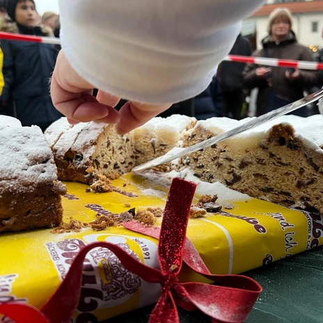 Na stole posypaném moučkovým cukrem se rukou krájí velký štolu.