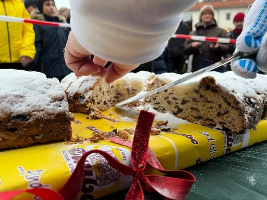 Oschatzer Weihnachtsmarkt - Weihnachten in der Region Leipzig Eine Hand schneidet einen großen Stollen auf einem Tisch, der mit Puderzucker bestreut ist.