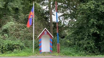 Grenzstation.jpg Kleine bunte Grenzstation mit rot-blauer Schranke und Flagge vor dicht bewachsenem Wald.