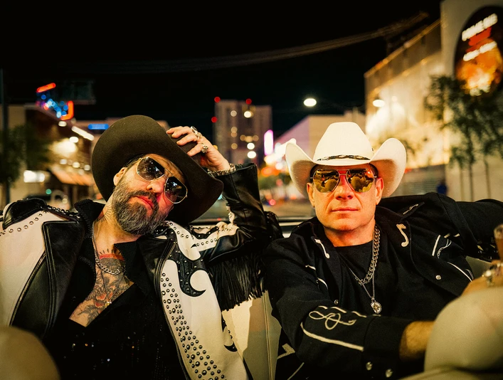 the-bosshoss-image.jpg Frontmen (Alec und Sascha) von The BossHoss sitzen mit Sonnenbrille und Cowboyhüten bei Nacht in einem Cabrio, im Hintergrund Häuser und Lichter