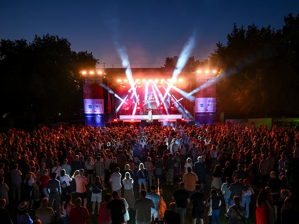 ray-dalton-muelheim-summer-open-air-2025-muega.jpg Bühne bei Nacht mit bunten Lichtern, umgeben von einem großen Publikum im Freien.