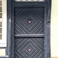 ©Bastian Ulrich - Haus auf der Arken 1 Schwarze Holztür mit kunstvollen Verzierungen unter einem weißem Schild mit der Aufschrift "Auf der Arken".