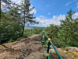 Viewpoint with green and yellow railings, trees and a view of the landscape.