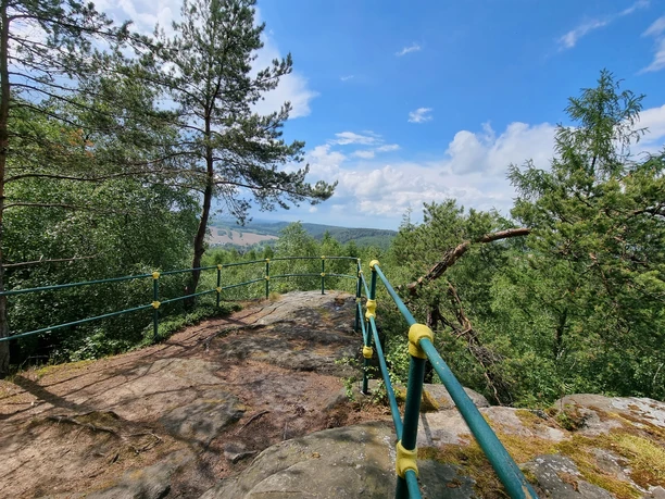 Uitkijkpunt met groen en geel hekwerk, bomen en uitzicht op het landschap.