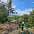 Hartenstein Aussichtspunkt mit grün-gelben Geländer, Bäumen und Blick auf eine Landschaft.Viewpoint with green and yellow railings, trees and a view of the landscape.Vyhlídka se zeleným a žlutým zábradlím, stromy a výhledem do krajiny.Punkt widokowy z zielonymi i żółtymi barierkami, drzewami i widokiem na krajobraz.Uitkijkpunt met groen en geel hekwerk, bomen en uitzicht op het landschap.Punto panoramico con ringhiere verdi e gialle, alberi e vista sul paesaggio.