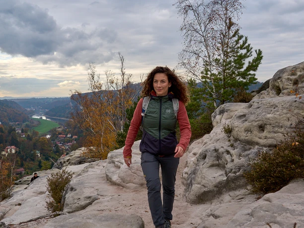 Vrouw wandelt op een rotsachtig bergpad met een bewolkte lucht op de achtergrond.