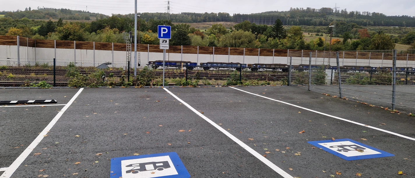 Wohnmobil-Parkplatz Bestwig Ein Parkplatz mit Bodenmarkierungen für Wohnmobile, dahinter Gleise und eine vegetationsreiche Umgebung.
