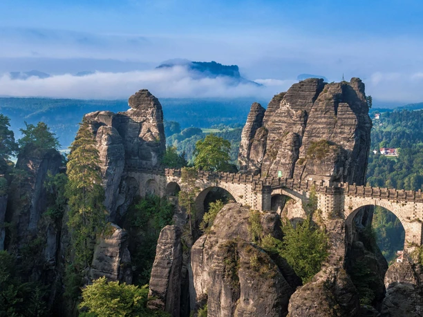 Bastei Brücke Felsformationen mit Brücke und Nebel über bewaldeten Bergen im Hintergrund.