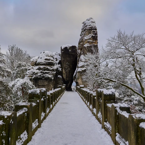 Basteibrücke Schneebedeckte Steinbrücke führt zwischen hohen Felsformationen hindurch.