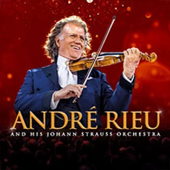 André Rieu spielt Geige vor rotem Hintergrund mit Orchester.