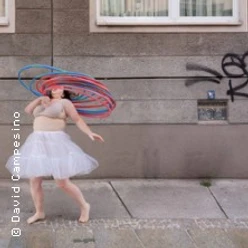 Person bewegt bunte Hula-Hoop-Reifen vor einer urbanen Wand mit Graffiti.