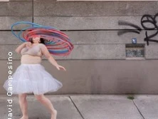 Person bewegt bunte Hula-Hoop-Reifen vor einer urbanen Wand mit Graffiti.