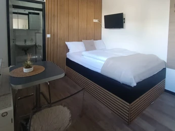 Schlafbereich des Appartements asado Moderner Schlafbereich mit Französischem Bett, Tisch mit 2 Stühlen, Fernseher an der Wand. Im hinteren Bereich Blick auf das separate Badezimmer