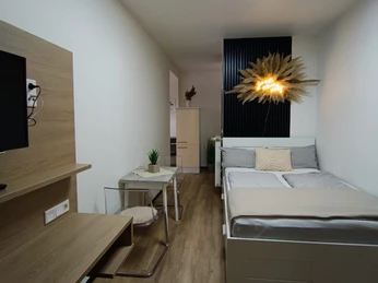 Schlafbereich des Appartement asado Moderner Schlafbereich mit Doppelbett, Holzfußboden, Schreibtisch, TV und dekorativer Wandbeleuchtung.