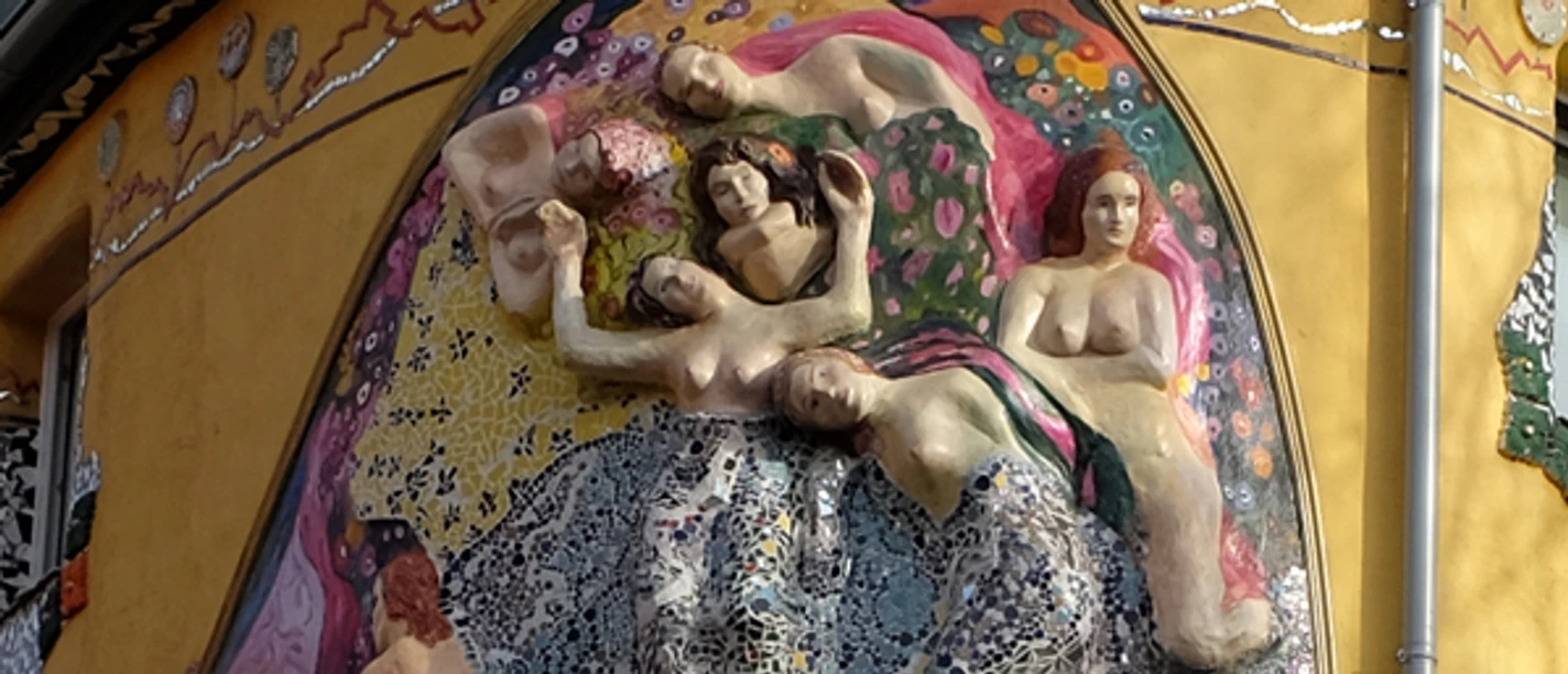 Liebe, Lust und Fisimatenten Eine detailreiche Mosaikskulptur an einer Gebäudewand zeigt mehrere ruhende Figuren.