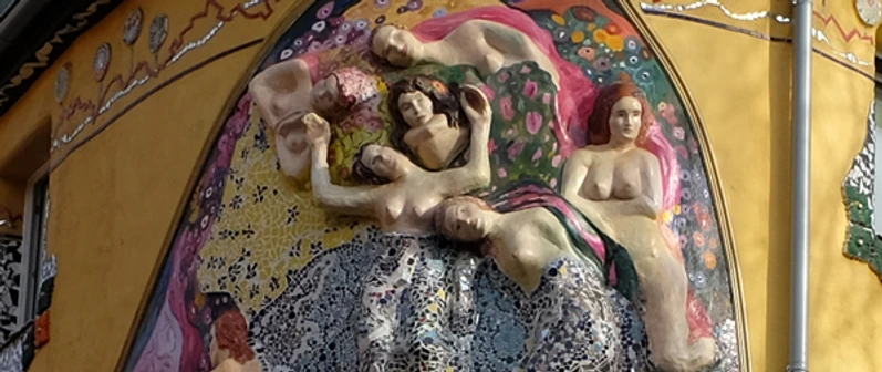 Liebe, Lust und Fisimatenten Eine detailreiche Mosaikskulptur an einer Gebäudewand zeigt mehrere ruhende Figuren.A detailed mosaic sculpture on the wall of a building shows several resting figures.