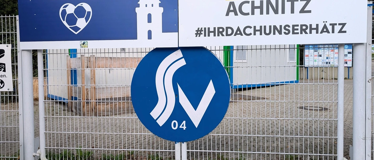 Walter-Mundorf-Stadion Eingang mit Werbetafeln und Siegburg-Logo in blau-weißer Farbgebung.