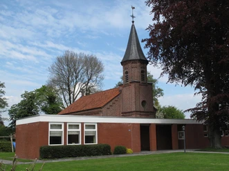Kath. Kirche Augustfehn, Außenansicht von vorn, Foto Kath. Kirche.JPG Backsteinkirche mit kleinem Spitzturm und rotem Ziegeldach, umgeben von Rasen und Bäumen.