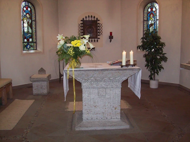 Kath. Kirche Augustfehn, Innenraum Altar, Foto Kath. Kirche.JPG Altarraum der katholischen Kirche Augustfehn mit Steinaltar, Blumen, Kerzen und Buntglasfenstern.