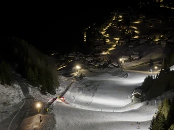 Descente éclairée au-dessus de Riederalp la nuit Beim Nachtskifahren Bettmeralp Riederalp leuchten die Skipisten oberhalb des Dorfes hell auf und bilden einen faszinierenden Kontrast zur dunklen BerglandschaftWhen skiing at night in Bettmeralp Riederalp, the ski slopes above the village light up brightly and form a fascinating contrast to the dark mountain landscapeLors du ski nocturne Bettmeralp Riederalp, les pistes de ski au-dessus du village s'illuminent et forment un contraste fascinant avec le paysage montagneux sombre.