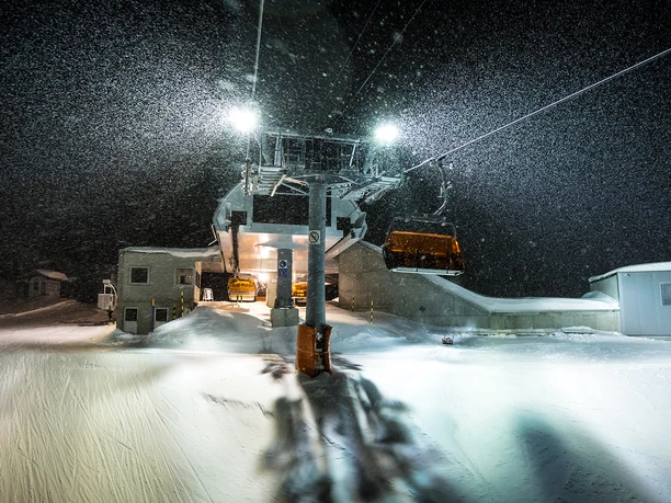 Snowfall and mood lighting for night skiing During night skiing in Bettmeralp Riederalp, thick snow falls at the middle station of the chairlift in the Aletsch Arena and glistens in the light of the lamps