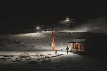 Night skiing at the Fieschertal family ski lift Night skiing Fieschertal shows the illuminated valley station of the Blaetz family ski lift with skiers and a cozy hut atmosphere in the Aletsch Arena