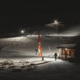 Ski nocturne au téléski familial de Fieschertal Le ski nocturne de Fieschertal montre la station inférieure éclairée du téléski familial Blaetz avec des skieurs et une ambiance chaleureuse dans un chalet de l'Aletsch Arena.