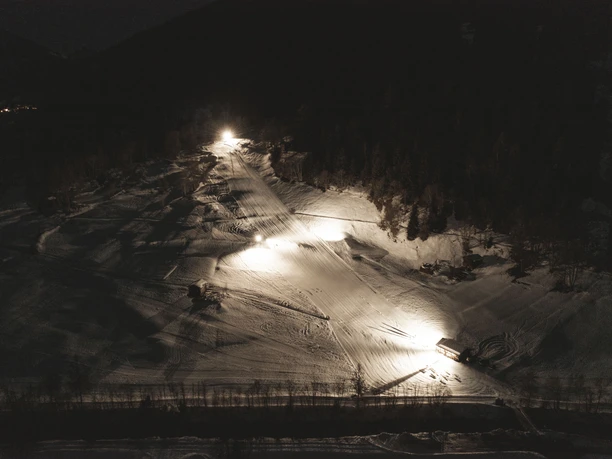 Le ski nocturne à Fieschertal vu du ciel Le ski nocturne de Fieschertal montre des pistes de ski et des surfaces enneigées éclairées par les airs sous un ciel clair dans l'Aletsch Arena hivernale.