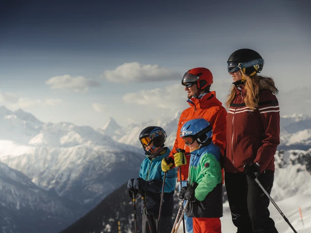 Familie geniesst Skitag mit Panorama in der Aletsch Arena Beim Familien Skipass Aletsch Arena geniesst eine Familie den Blick auf die verschneiten Walliser Alpen während einer Skitour bei sonnigem Wetter