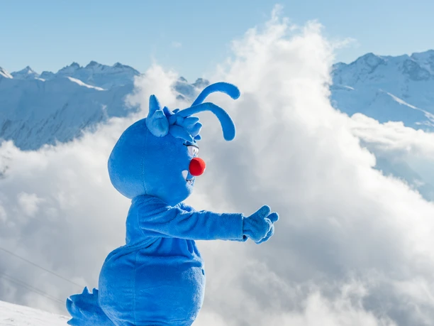 Gletschi mascot welcomes families to the Aletsch Arena With the Aletsch Arena family ski pass, the blue mascot Gletschi greets skiers with a smile against a snowy Alpine backdrop in winter