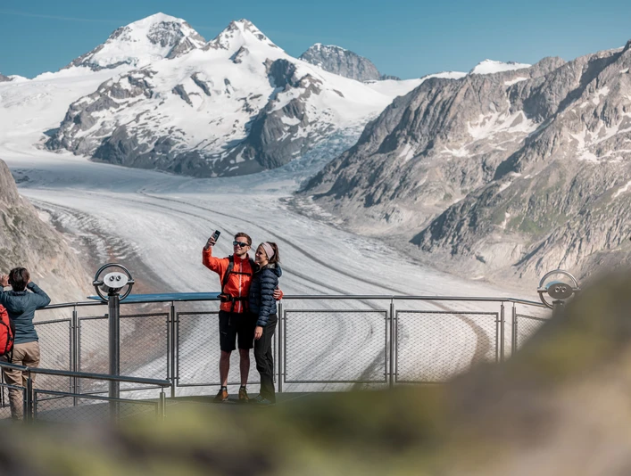 Selfie mit Aussicht am View Point Eggishorn Das View Point Package Aletsch zeigt ein Paar beim Selfie auf dem Eggishorn mit spektakulärer Aussicht auf den Grossen AletschgletscherThe View Point Package Aletsch shows a couple taking a selfie on the Eggishorn with spectacular views of the Great Aletsch GlacierLe forfait View Point Aletsch montre un couple en train de prendre un selfie sur l'Eggishorn avec une vue spectaculaire sur le grand glacier d'Aletsch.