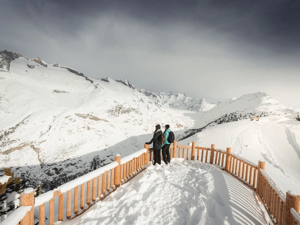 Winterpanorama vom View Point Hohfluh auf den Aletschgletscher Das View Point Package Aletsch zeigt zwei Winterwanderer auf dem Aussichtspunkt Hohfluh mit Blick über den verschneiten Grossen Aletschgletscher