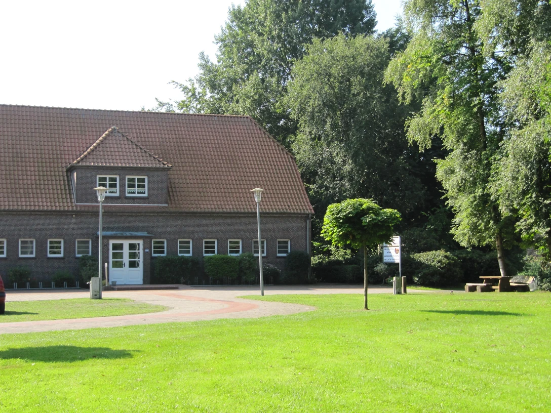 Bokler Schule.JPG Backsteingebäude mit rotem Dach, umgeben von grüner Wiese und Bäumen bei sonnigem Wetter.